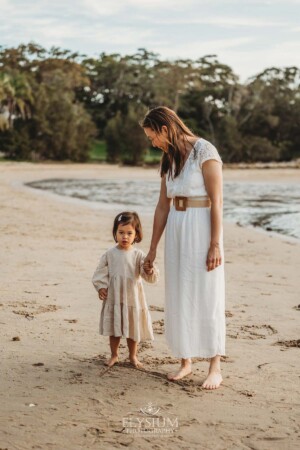 A mother holds the hand of her little girl as they stand on the waters edge at sunset