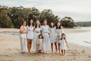 A family stand on the sand at a beach with the sun setting behind them