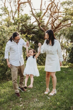 Parents swing their little girl between them as they stand in a bushy field