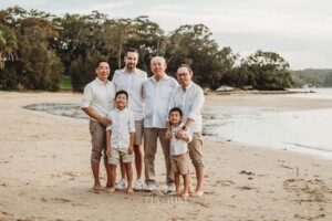 A family stand on the sand at a beach with the sun setting behind them