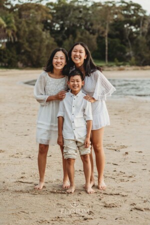 Three kids stand cuddling together on a beach at sunset
