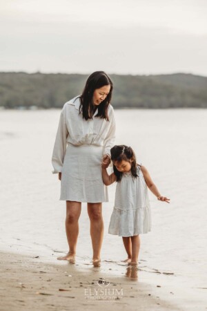 A mother and daughter dip their toes in the water at the beach