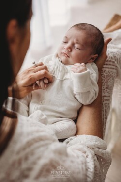 A mother wearing a white lace dress cradles her newborn baby in her lap