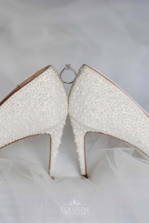 The brides wedding ring balances between her white high heels