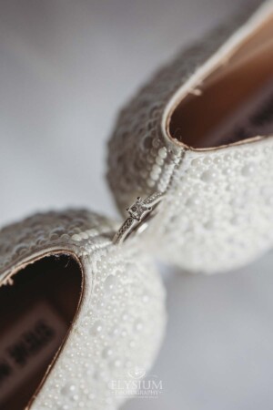 The brides wedding ring balances between her white high heels