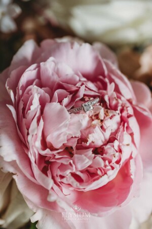 The wedding rings sit in the petals of a pink peony in the bridal bouquet