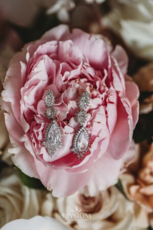 The bride's earrings sit in the petals of a pink peony in the bridal bouquet