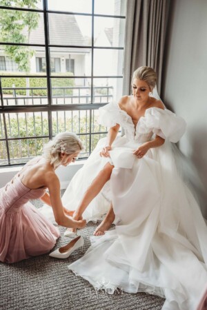 A bridesmaid helps the bride put on her shoes