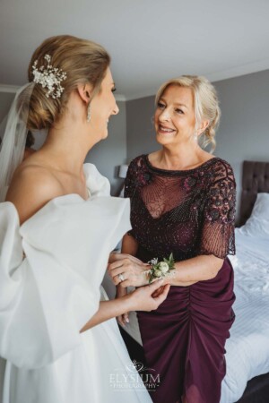 A bride places a corsage on her mothers wrist