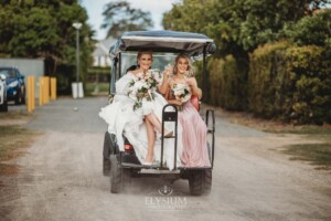 A bride sits with her bridesmaid on the back of a buggy at Burnham Grove