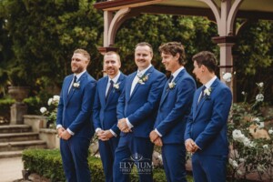 Groomsmen stand laughing in front of the Burnham Grove homestead