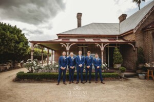 Groomsmen stand in front of the historic Burnham Grove homestead