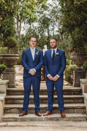 Groomsmen stand on stone steps in a lush green venue garden in Camden