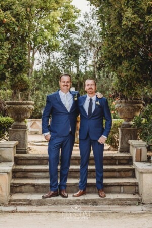 Groomsmen stand on stone steps in a lush green venue garden in Camden