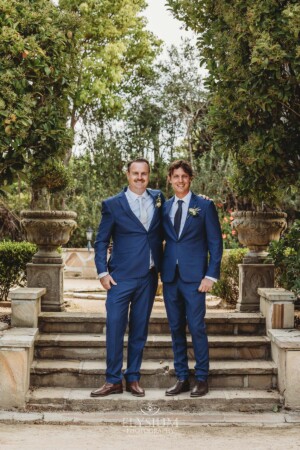 Groomsmen stand on stone steps in a lush green venue garden in Camden