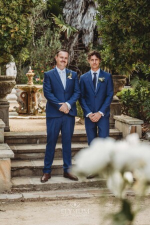 Groomsmen stand on stone steps in a lush green venue garden in Camden