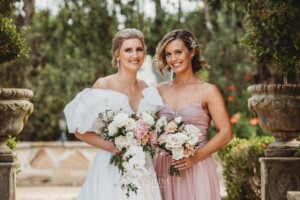 Bridal party pose for photos in front of green hedges