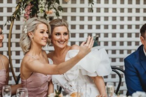 A bride and her sister take a selfie at the wedding reception