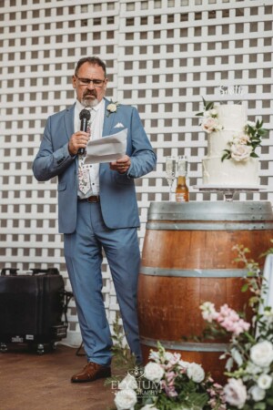 The brides father stands next to the wedding cake and makes his speech