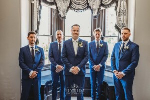 Groomsmen stand in the homestead at Burnham Grove