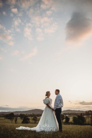 A bride and groomhold hands as the sun sets behind them overlooking Camden