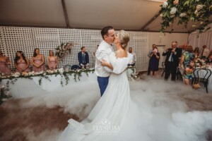 A bride and groom kiss during their first dance surrounded by dry ice fog