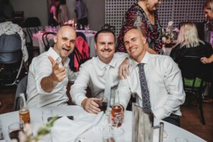 A groom sits with wedding guests and poses for a photo