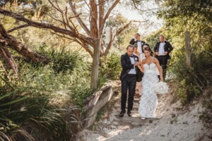 A couple walk down onto a beach with their wedding party on a sunny day