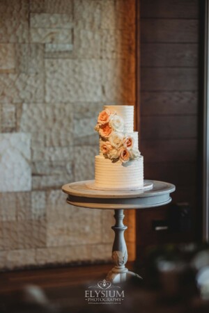 A white wedding cake covered with floral details in peach tones sits on a table