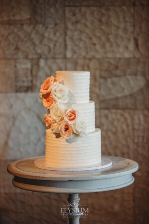 A white wedding cake covered with floral details in peach tones sits on a table