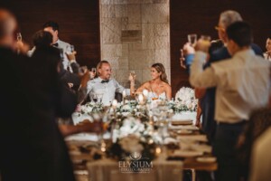 Wedding guests raise their glasses to toast the bride and groom as they sit at the bridal table