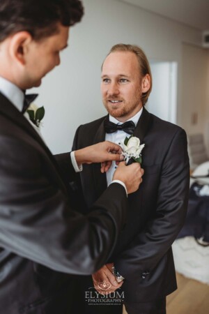 A groomsman helps the groom with his buttonhole flower as they get ready for the wedding