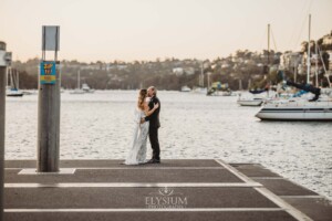 A wedding couple stand on a pier as the sun sets behind them over Sydney Harbour