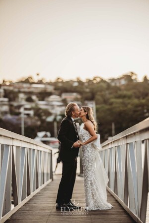 A wedding couple stand on a pier and kiss as the sun sets behind them