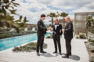 A groom shares a toast with his groomsmen beside a blue pool before they head to the wedding ceremony