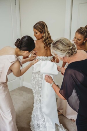 The bridal party help the bride into her gown before the wedding