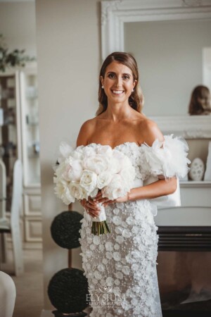 A bride wearing a textured white wedding dress holds a white bouquet of flowers