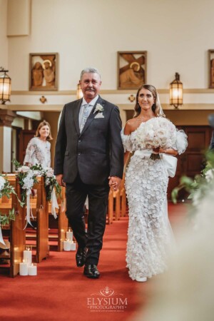 A bride walks with her father down the wedding aisle in the chapel of Loreto Normanhurst
