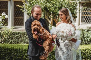 A bride and groom pat their dog as they stand in front of Loreto Normanhurst after their wedding ceremony