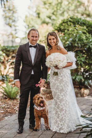 A bride and groom walk their dog through the gardens of Loreto Normanhurst after their wedding ceremony
