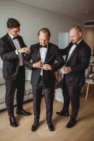 Groomsmen help the groom into his jacket as they prepare for his wedding