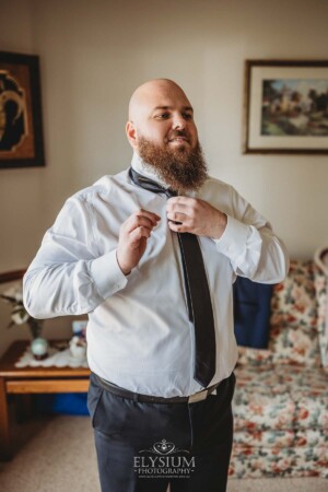 A groom adjusts his tie as he gets ready for his wedding