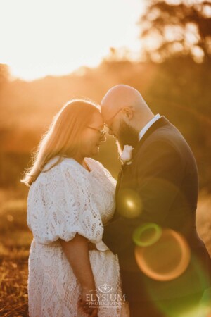 A bride and groom stand with their foreheads together in the warm orange sunset after their wedding
