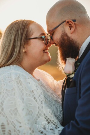 A bride and groom stand with their noses pressed together in the warm orange sunset after their wedding