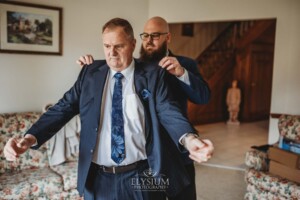 A groom helps his father with his jacket as they prepare for the wedding