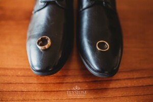 A groom's wedding rings sit on the tip of his black shoes
