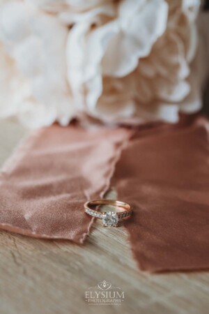 An engagement ring sits on a pink silk ribbon wrapped around a bridal bouquet