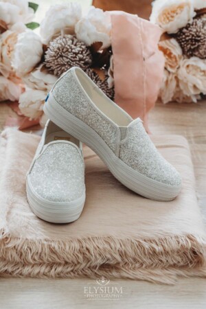 White glittery bridal sneakers sit on a soft pink shawl