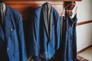 Navy blue wedding suits and a dress hang from a timber fireplace mantle