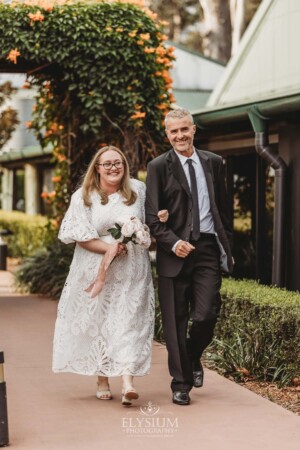 A bride walks with her father down the aisle towards her wedding ceremony